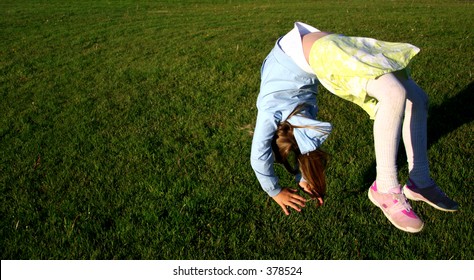 Girl In Mid-air Doing Somersault On Green Grass