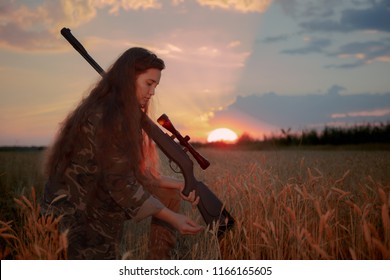 girl in military uniform sits in a field on the grass amidst wheat with weapon on the shoulder, beautiful sunset in field, beautiful colors