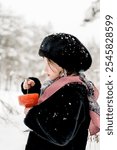 A girl in a mink coat and hat holds a glass of red caviar in her hand and eats it.