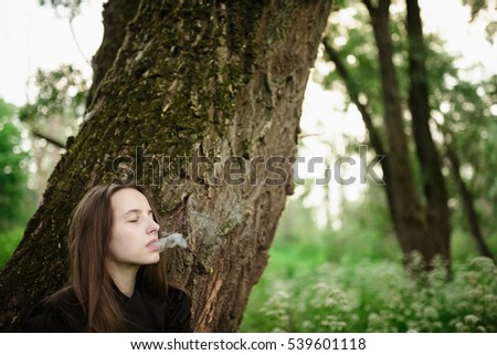 girl model produces smoke from the mouth in the woods on a background of wood