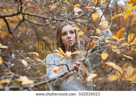 girl model stands among walnut branches, pushes their hands away. He looks to the side and upwards. dressed in gray knitted sweater. Cold autumn yellow