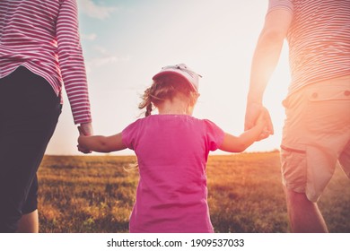 Girl with mother and father holding hands on the nature. Child with parents outdoors