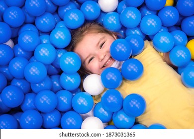 girl in multi-colored ball in children's playgroup. the child smiles, hiding in the balls