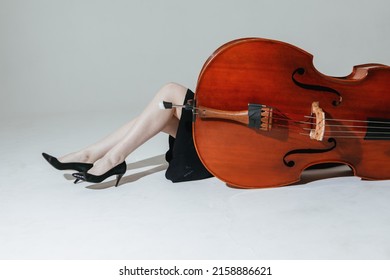 Girl musician in black dress poses with the double bass against different backgrounds.