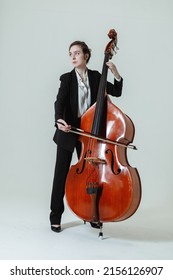 Girl musician with long hair in black suit and white shirt plays with the double bass against the white background.