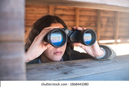 Girl in nature with binoculars doing outdoors activities . Searching, sightseeing , tourism, discover and birdwatching concept.