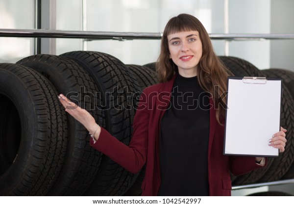 the girl near the car wheels stands\
and advertises the car tires with a white and empty\
sign