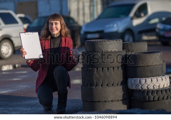 the girl near the car wheels stands and advertises\
the car tires with a white and empty sign. Restoration of the tread\
of tires.