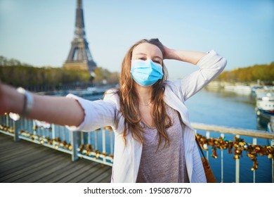 Girl near Eiffel tower in Paris wearing mask and taking selfie or recording video blog during coronavirus outbreak. Pandemic and lockdown in France. Tourist spending vacation in France during pandemic