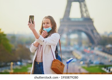 Girl near Eiffel tower in Paris with half-removed face mask during coronavirus outbreak, taking selfie or recording video blog. Pandemic and lockdown in France. Tourist spending vacation in France
