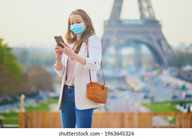Girl near Eiffel tower in Paris wearing mask and taking selfie or recording video blog during coronavirus outbreak. Pandemic and lockdown in France. Tourist spending vacation in France during pandemic