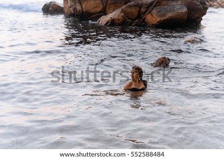 Girl in ocean water near the beach in front of big stone 