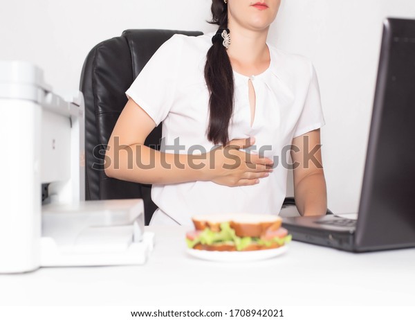 Girl office worker near which lies a sandwich holding
on to a stomach in which there is pain and inflammation in the
stomach. Concept of indigestion and malnutrition in office workers,
gastritis and