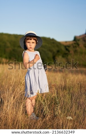 A girl with an old camera in her hand among the grass in a meadow.                               