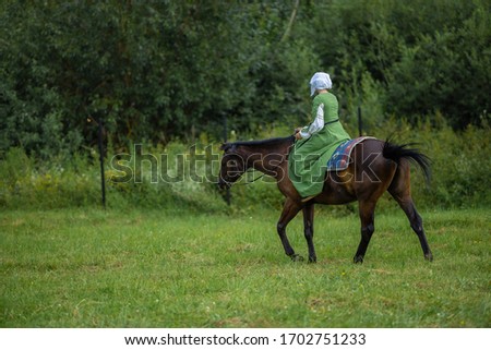 A girl in an old long dress rides a horse in the forest