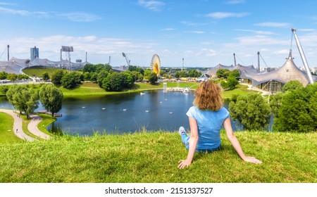 Girl in Olympic Park, Munich, Germany. Young woman sits on grass in Munich amusement district, person rests in summer. This place is tourist attraction of Munchen city. Travel people in Europe.