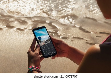 Girl on the beach holding a smartphone with Adobe Photoshop Lightroom app on the screen. Rio de Janeiro, RJ, Brazil. March 2022.