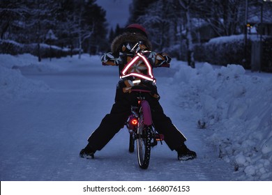 Girl on a bicycle in a winter evening. Light is reflected from clothing reflectors and bicycle wheels. Safe cycling in the dark time.