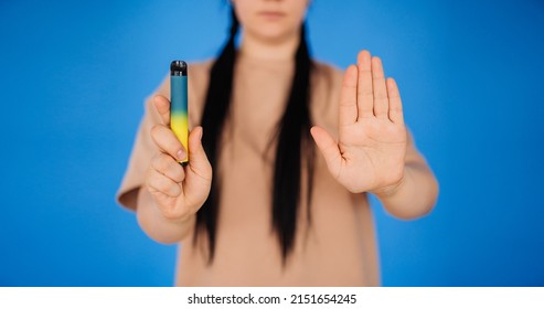 a girl on a blue background holds a disposable cigarette in one hand and shows a stop to smoking with the other hand. the concept of a healthy lifestyle.