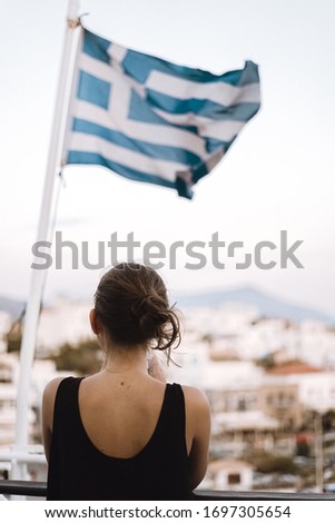 Girl on a ferry taking a photo with her phone, whit the greek flag in the background