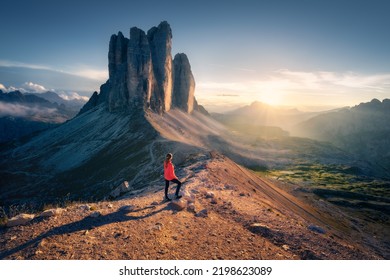 Girl on the mountain peak and amazing high rocks at colorful sunset in Tre Cime, Dolomites, Italy. Landscape with young woman on trail, cliffs, stones, blue sky and sun in autumn. Trekking and hiking - Powered by Shutterstock