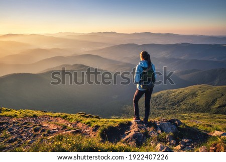 Girl on mountain peak with green grass looking at beautiful mountain valley in fog at sunset in summer. Landscape with sporty young woman, foggy hills, forest, sky. Travel and tourism. Hiking Foto stock © 