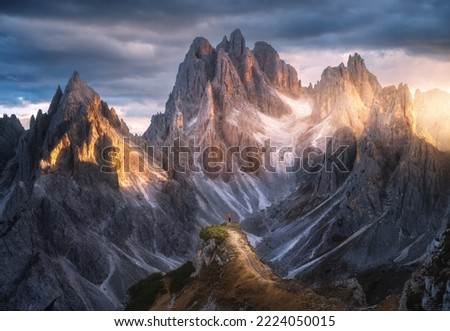 Girl on the mountain peak and high rocks at colorful sunset in autumn. Tre Cime, Dolomites, Italy. Colorful landscape with woman on trail, cliffs, grass, cloudy sky in fall. Hiking. Aerial view