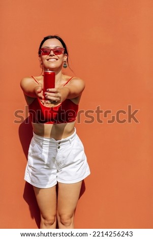 A girl on an orange background with a red tin can in her hands. Cheerful girl, advertising shooting. High quality photo