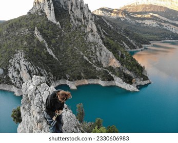 girl on the peak and on top of mont rebei, in catalonia. at the end of a via ferrata, climbing and risk activity. the background, an incredible and majestic blue lake and a rock ridge, forests and mou