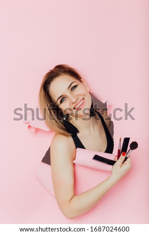 girl on a pink background with a camera and makeup brushes.Pin up woman looking through paper. copy space.Breaking paper. Sale. Discount