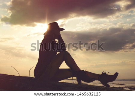 Girl on the river sits on a wooden log in the sunset