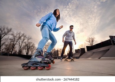 Girl On Rollerblades And Boy On Skateboard In Skate Park