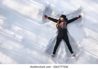 A Girl On The Snow Shows An Angel. Spreading Arms. Top View. Drone. Smile. Happy.