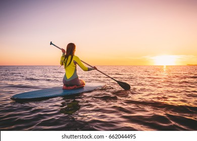 Girl on stand up paddle board, quiet sea with warm sunset colors. Relaxing on ocean