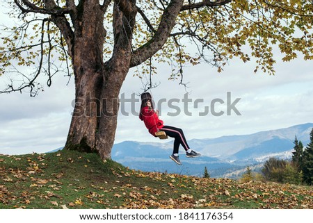 Girl on a swing on vacation overlooking the mountains and forests. Young lonely traveler girl sitting on a swing in a red raincoat on a background of beautiful nature.
romantic girl on swing, dream 
