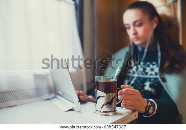 Girl on a train with a\
laptop computer watching a movie and drinking tea. Traveling in an\
empty car