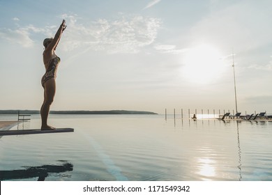 Girl on the trampoline before jumping into the open pool. Woman standing on diving board, preparing to dive - Powered by Shutterstock