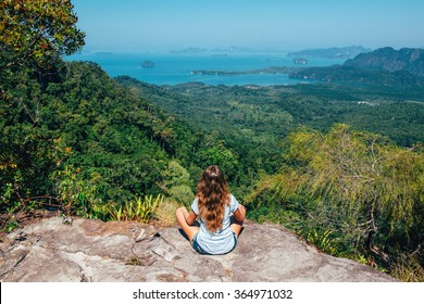 Girl on the view point of the mountain, sitting back to the camera, concept of freedom and traveling. Traveler enjoying the landscape from mountain in Tab Kak Hang Nak Nature Trail, Krabi, Thailand