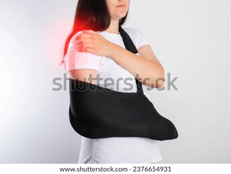 A girl on a white background with a black supporting medical bandage after a dislocation of the shoulder joint and a bone fracture. Rehabilitation after injury, orthopedics.