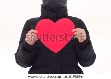 The girl on a white isolated background holds in front of her a big red horse. Figure without a face in black winter clothes. Valentine's Day stock photo with empty space for your text.