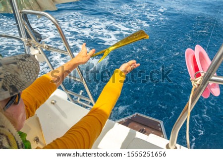 Girl on a yacht gutting freshly caught dorado fish (mahi-mahi, Coryphaena,  dolphinfish). White deck of a cruise sailing yacht, blue sea and freshly caught fish fillet. Sea fishing in Phuket, Thailand