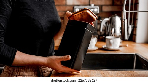 Girl opening tea black metal jar at kitchen to prepare hot natural beverage. Woman hands holding herbal drink container at home - Powered by Shutterstock