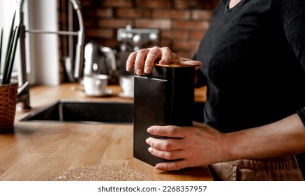 Girl opening tea black metal jar at kitchen to prepare hot natural beverage. Woman hands holding herbal drink container at home - Powered by Shutterstock