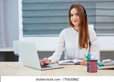 Girl Operator Working Behind A Laptop On The Desktop Looking Straight