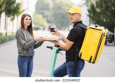 Girl Ordered Delivery Of Pizza. Attractive Young Delivery Guy Holding Box With Hot Pizza And Cup With Hot Drink Coffee. Friendly Delivery Man Handing Pizza To A Customer.