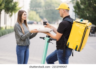 Girl Ordered Delivery Of Pizza. Attractive Young Delivery Guy Holding Box With Hot Pizza And Cup With Hot Drink Coffee. Friendly Delivery Man Handing Pizza To A Customer.