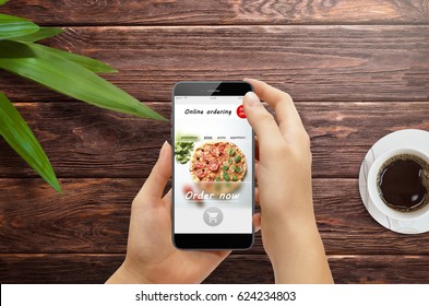 Girl Ordering Pizza Online On Smartphone, With Table And Coffee And Plant In Background