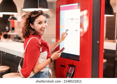 A girl orders food and lunch at a fast food restaurant using a self-service kiosk or a terminal with a screen. Modern commerce equipment