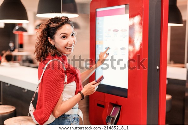 A girl orders food and lunch at a fast food\
restaurant using a self-service kiosk or a terminal with a screen.\
Modern commerce equipment