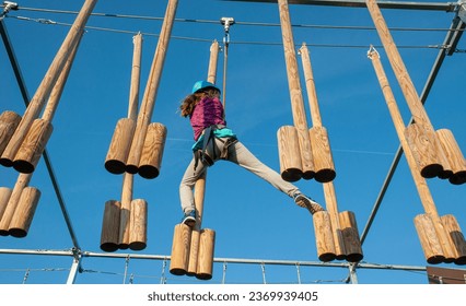 A girl overcomes obstacles in an adrenaline park. The girl tries to step on the next hanging wooden step. - Powered by Shutterstock